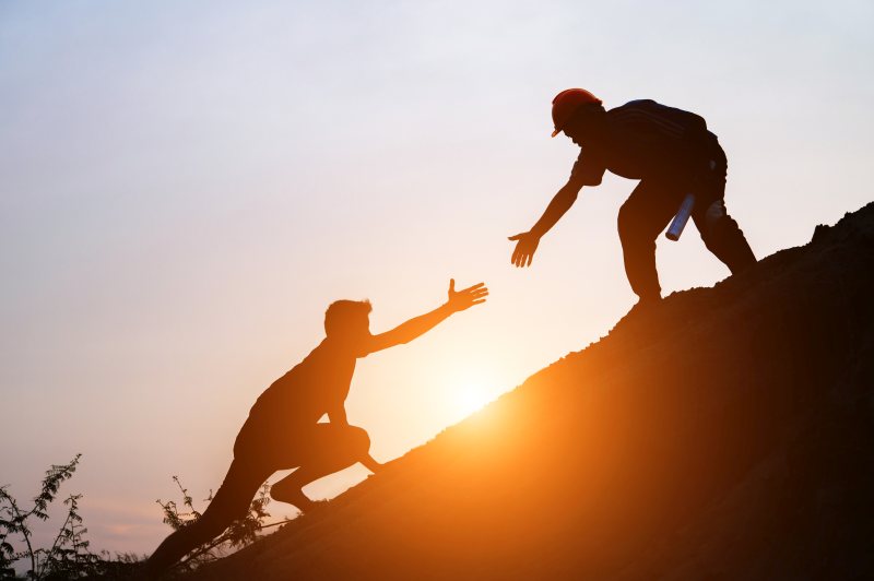 Silhouetted figures helping each other climb a hill at sunset. Teamwork, support, and collaboration.